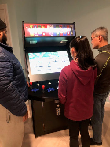 Three People Playing A Marvel-themed Arcade Machine